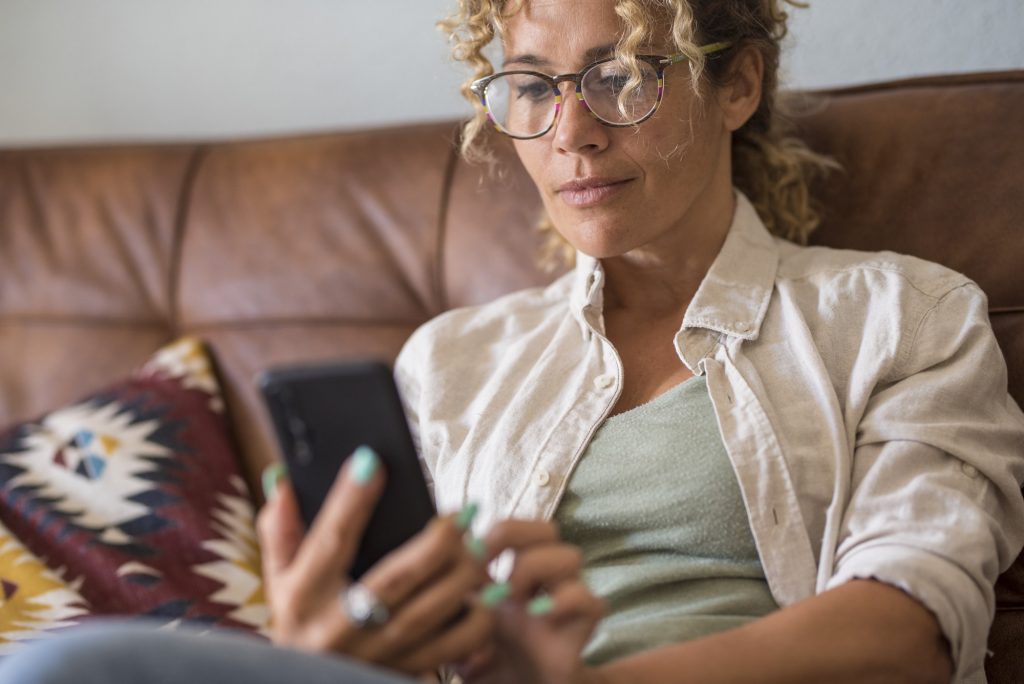Close up of woman using modern smart phone at home sitting on the sofa enjoying internet